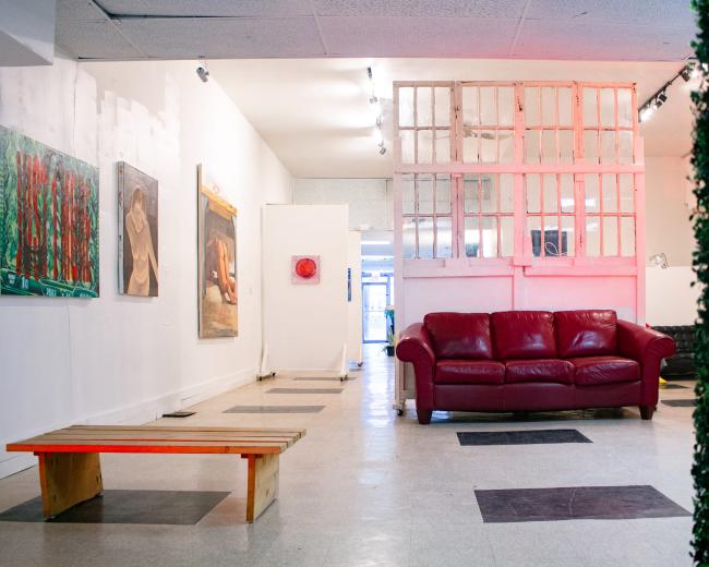 The image shows an art gallery with a red couch and artwork hanging on the walls, illuminated by bright lighting.