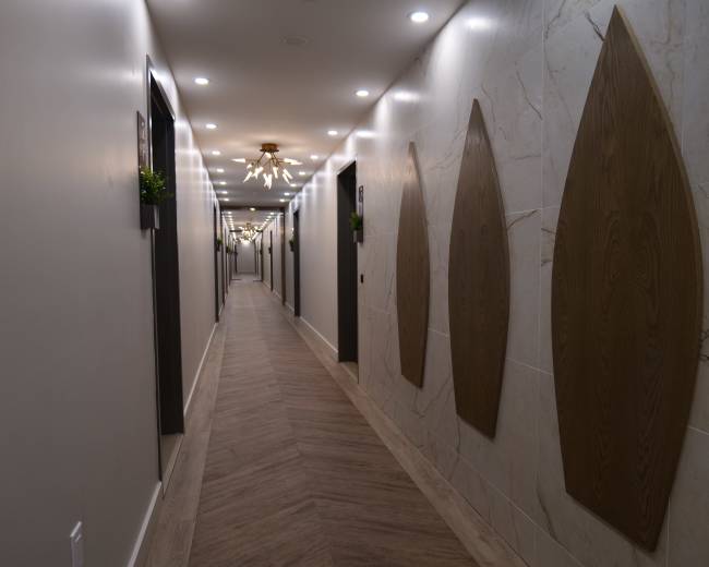 A well-lit hotel corridor features decorative wood paneling and modern light fixtures along the walls.