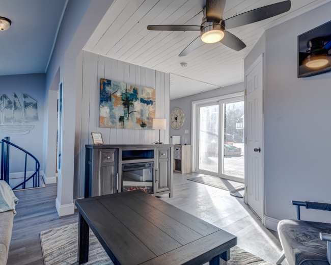 A modern living room features a gray sofa, a dark wood coffee table, and a view of a patio through sliding glass doors.