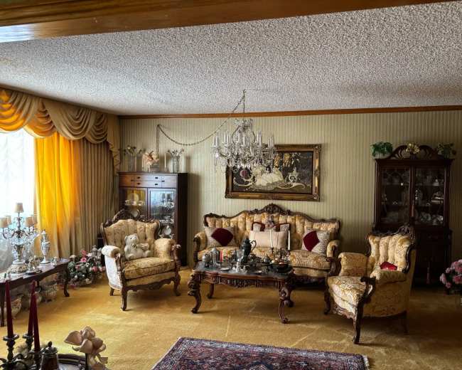 The image shows a formal living room featuring ornate furniture, a chandelier, and a combination of decorative items and floral arrangements.