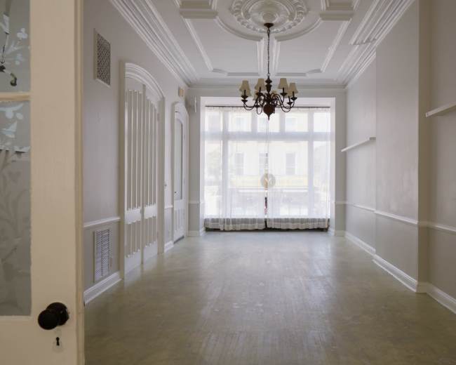 The image shows an empty, well-lit room with a chandelier, large windows, and decorative ceiling details.