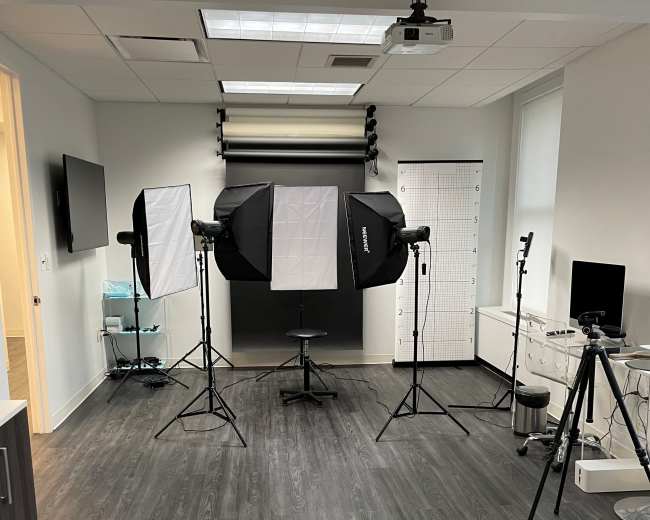 The image shows a photography studio with lighting equipment, a backdrop, and various cameras arranged for a photo shoot.