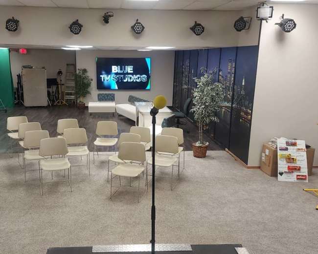 A studio setup with rows of chairs facing a microphone stand and a display screen that reads "BLUE TWIST STUDIOS," with green and black backdrops in the background.