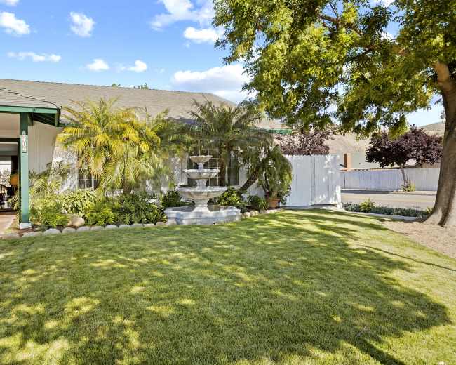 A well-maintained front yard features a fountain surrounded by greenery and a lawn in front of a single-story house.