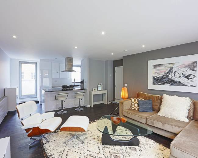 A modern living room with a sectional sofa, a glass coffee table, and an open kitchen area featuring a breakfast bar and stylish appliances.