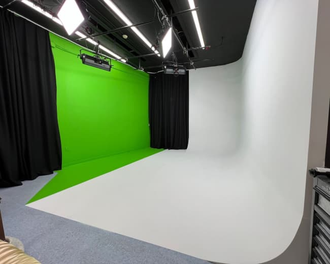 A photography studio featuring a green screen on one side and a white seamless backdrop on the other, with lights and curtains around the space.