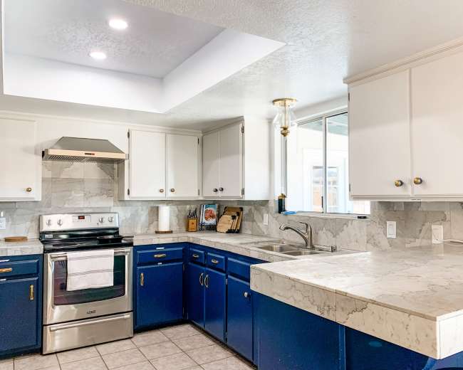 The image shows a kitchen with blue cabinets, a marble countertop, and stainless steel appliances.