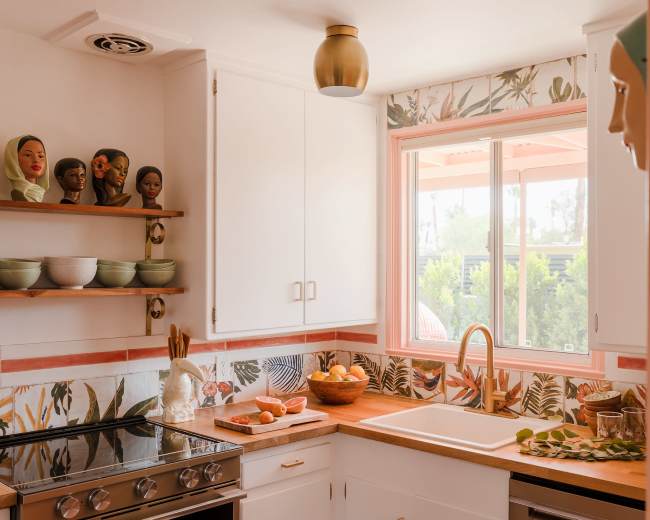 A bright kitchen features a stove, a wooden countertop with decorative bowls, and a window showcasing surrounding greenery.