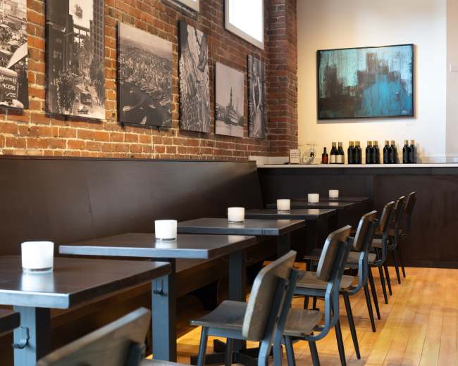 The image shows a modern café with wooden tables and chairs arranged along a brick wall adorned with black-and-white photographs.