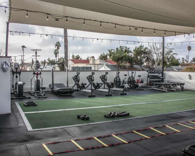 A rooftop gym with various exercise equipment, including treadmills, stationary bikes, and free weights, under a large canopy.