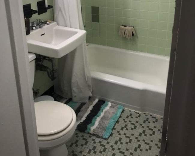 A small bathroom features a bathtub, toilet, and sink with green tile walls and a shower curtain.