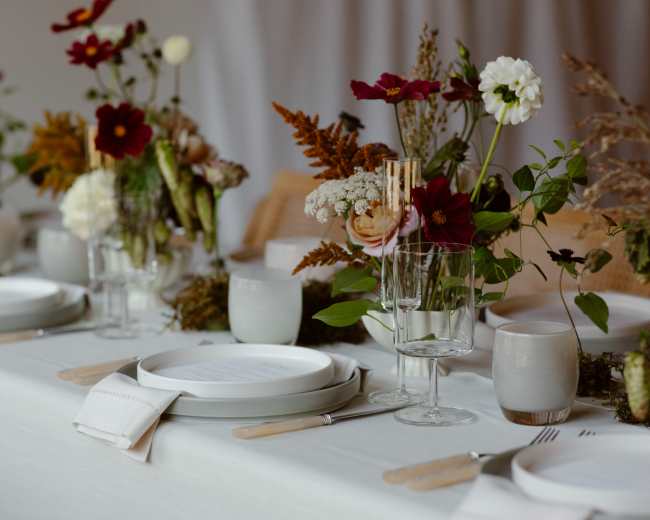 A beautifully arranged dining table features elegant dishware and vases filled with colorful flowers, set for a meal.