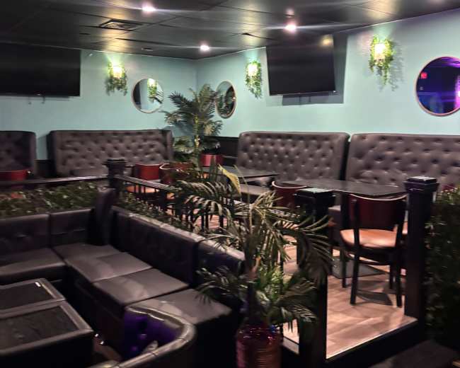 The image shows a modern lounge area with black leather seating, circular mirrors on the walls, and decorative plants.