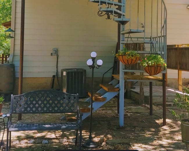 A spiral staircase leads from a patio area to a second-floor deck of a house.