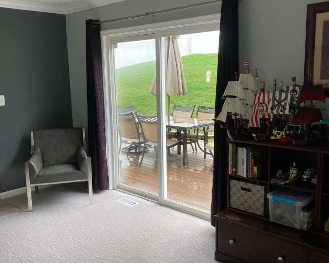 A living room with a gray wall, a chair, and a view of a patio through sliding glass doors.
