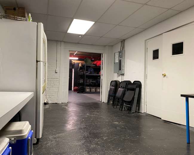 A long hallway leads to a storage area with stacked shelves and chairs lined up against the wall.