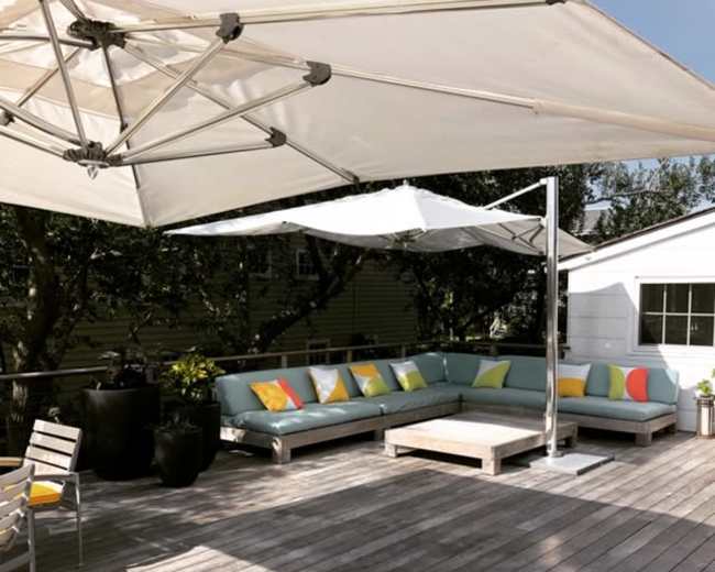 A covered outdoor seating area features a sectional sofa with colorful cushions and a coffee table on a wooden deck.