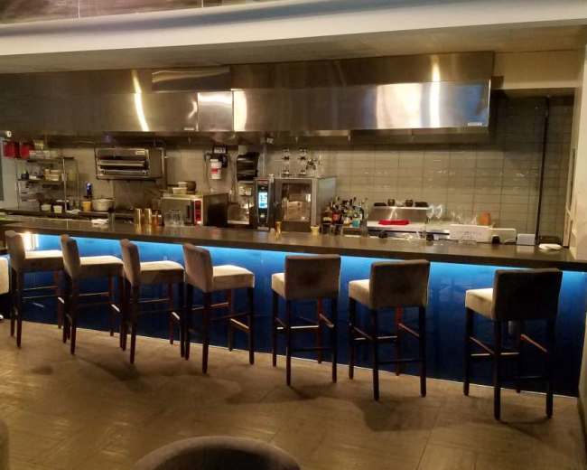 A sleek bar area with high stools is positioned in front of an open kitchen, featuring a modern design and ambient lighting.