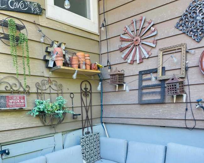 A corner seating area with a gray couch and glass table is arranged against a wooden wall adorned with decorative items and plants.