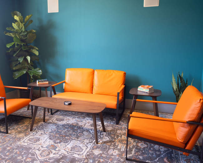 A cozy lounge area features orange seating, a wooden coffee table, and decorative plants against a teal wall.