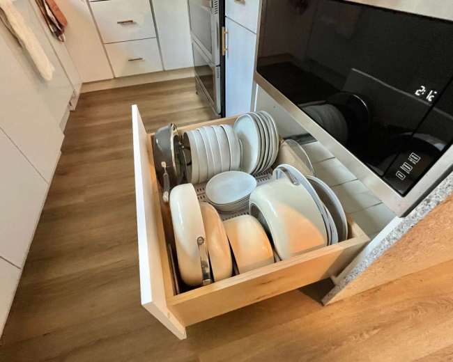 A kitchen drawer is open, containing neatly stacked plates, bowls, and cookware.