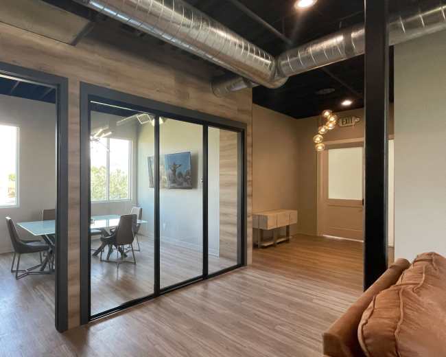 The image shows a modern office space featuring a glass-walled conference room with a table and chairs, separated from a lounge area with a couch.