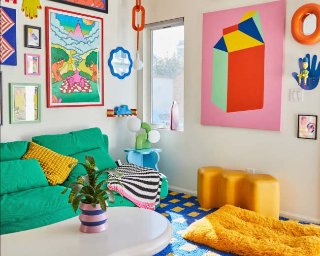 The room features a colorful decor with a green sofa, vibrant artwork on the walls, and a patterned blue rug.