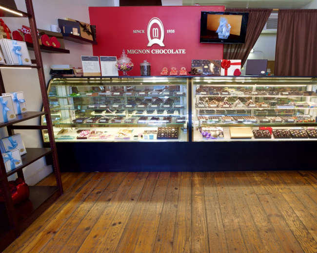The image shows the interior of a chocolate shop with a display case filled with various types of chocolates and confections.