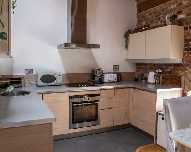The image shows a modern kitchen featuring light wood cabinetry, a stainless steel oven, a microwave, and a sleek countertop.