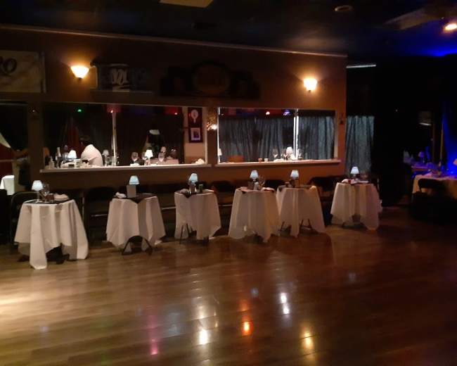 A dimly lit restaurant features several tables set with white tablecloths and centered around a mirrored wall.