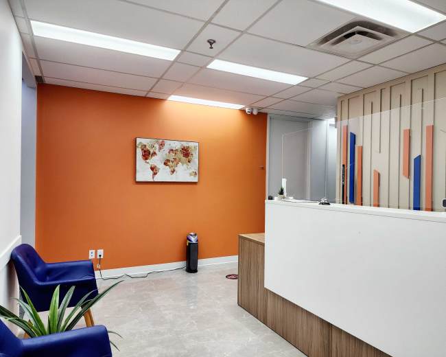The image shows a modern reception area with orange walls, a white reception desk, blue chairs, and a world map painting.