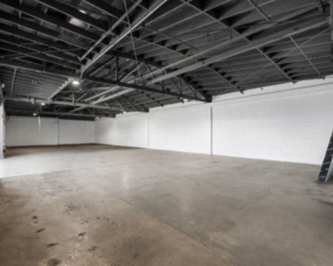 The image shows a large, empty industrial space with a concrete floor and exposed metal beams overhead.