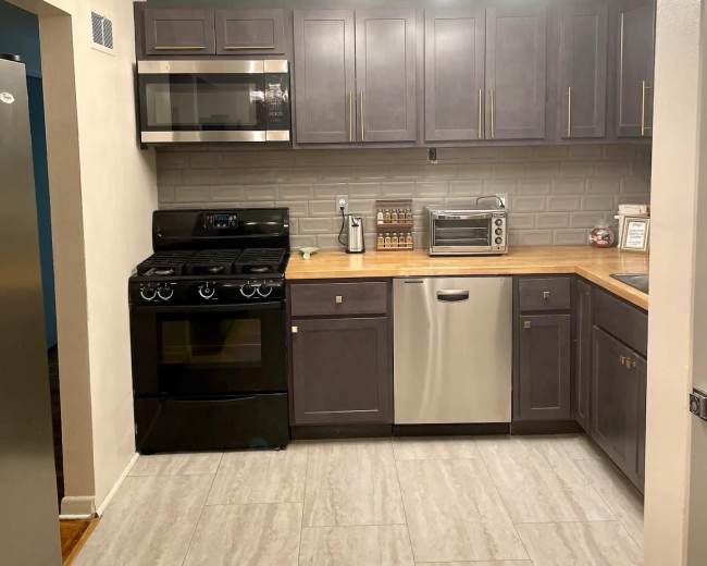 The kitchen features dark cabinetry, a stainless steel dishwasher, a black stove, and a countertop with a microwave and decorative jars.