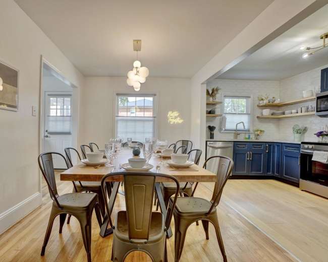 A dining area with a wooden table set for a meal is adjacent to a kitchen featuring blue cabinets and modern appliances.