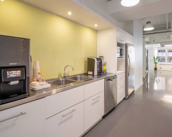 A modern kitchen area featuring stainless steel appliances, a double sink, and a countertop with a coffee machine against a green accent wall.