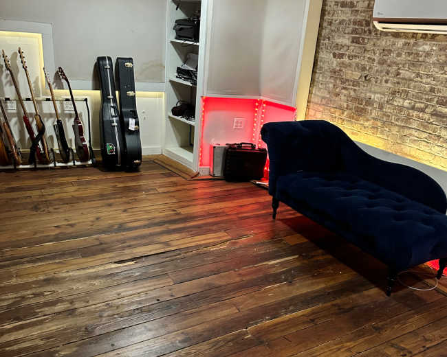 A room with wooden floorboards, a dark blue couch, and multiple guitars displayed against a wall with ambient lighting.