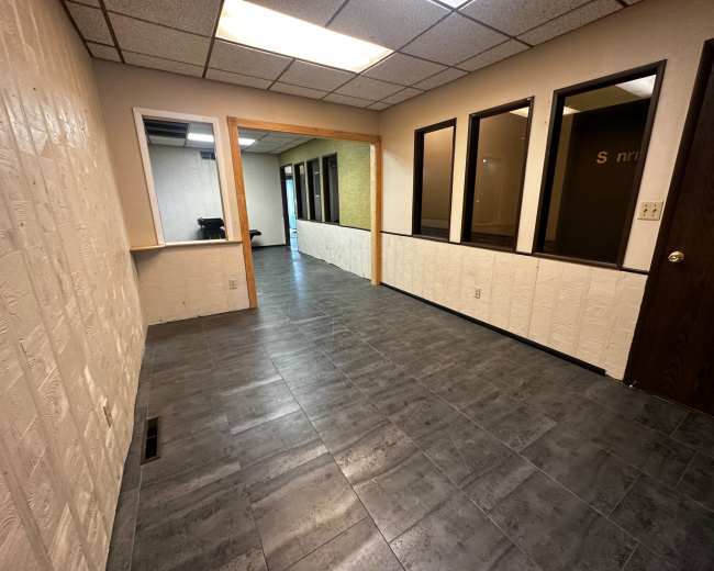 The image shows a hallway in an office building with tiled flooring and access to several rooms on one side.