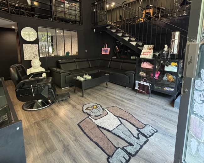 The image shows a modern, two-level interior of a black-themed café or lounge, featuring a staircase, seating area with black couches, and decorative elements.
