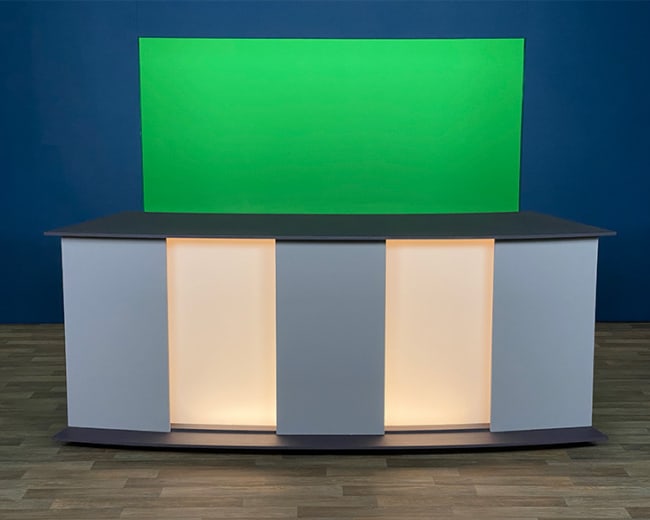 A modern studio set features a gray countertop with illuminated panels and a green backdrop.