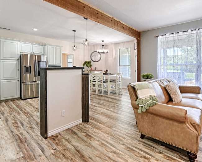The image shows a modern, open-concept living area featuring a leather sofa, a dining table, and large windows that allow natural light to fill the space.
