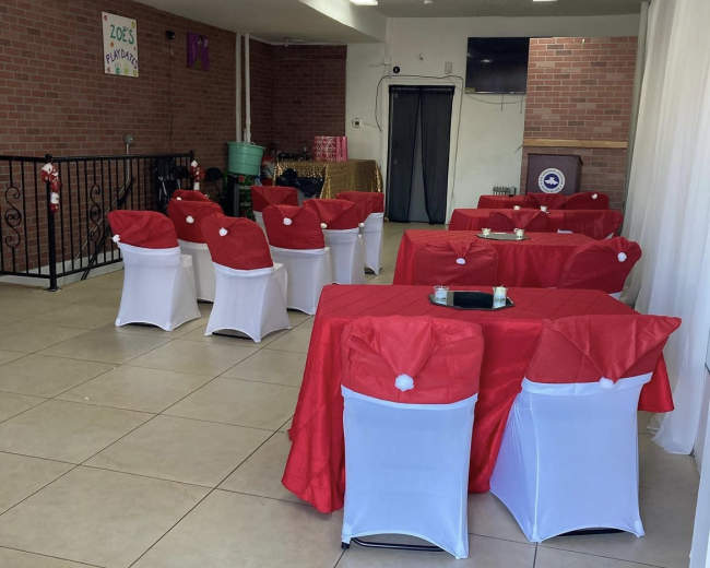 A decorated indoor space with tables covered in red tablecloths and white chair covers, arranged for an event.