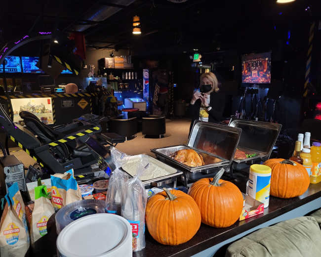 A table with food containers and pumpkins is set up in a gaming lounge, with gaming machines and screens visible in the background.