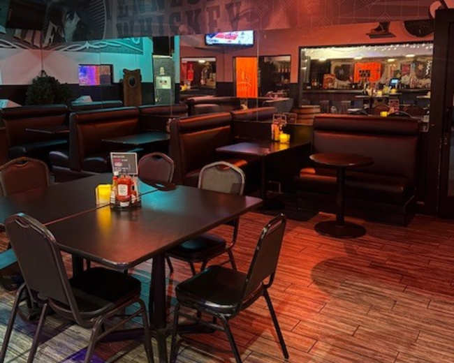 The image shows an interior view of a restaurant with black booth seating, a table set for dining, and soft lighting.