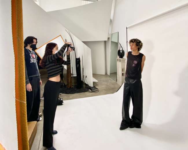 A photographer takes pictures of a model in a studio setting, while two assistants observe nearby.