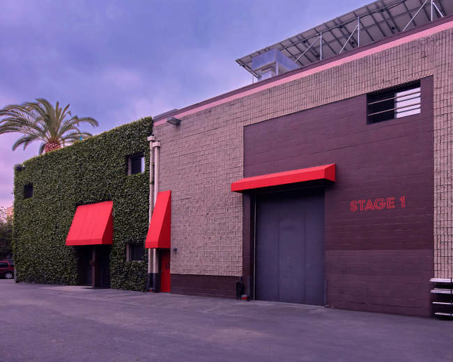 The image shows a soundstage building labeled "STAGE 1," with palm trees and red awnings on the exterior.