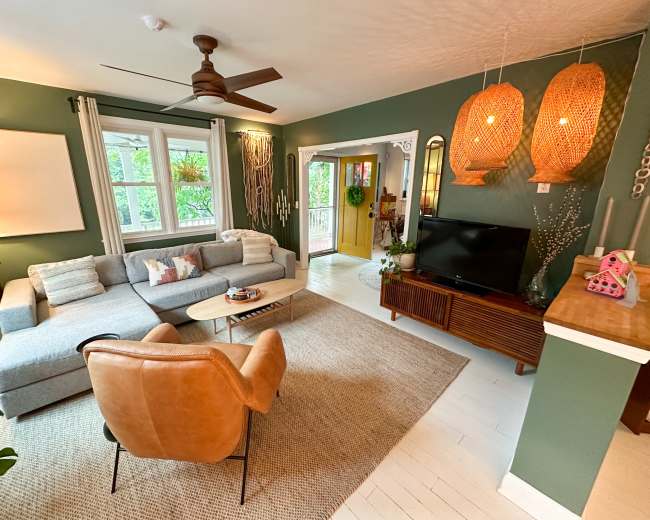 The living room features a gray sectional sofa, a brown leather armchair, and a television on a wooden stand, with green walls and woven pendant lights.