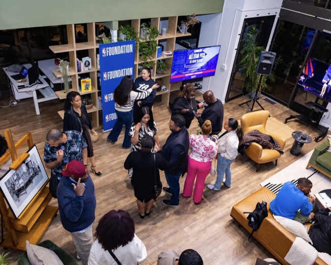 A group of people converse and socialize in a modern indoor space furnished with plants and stylish seating arrangements.