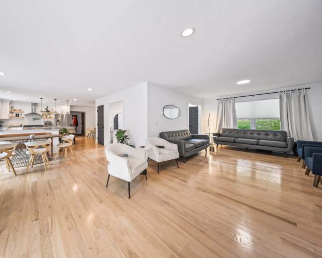 The image shows a spacious living area with hardwood floors, a seating arrangement, and a dining space connected to a kitchen.
