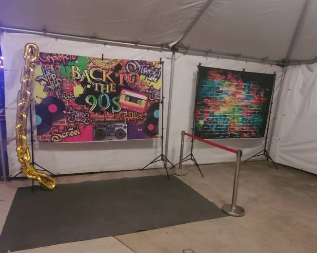 A decorated area inside a tent featuring a "Back to the 90s" theme with vibrant banners and a cordoned-off section.