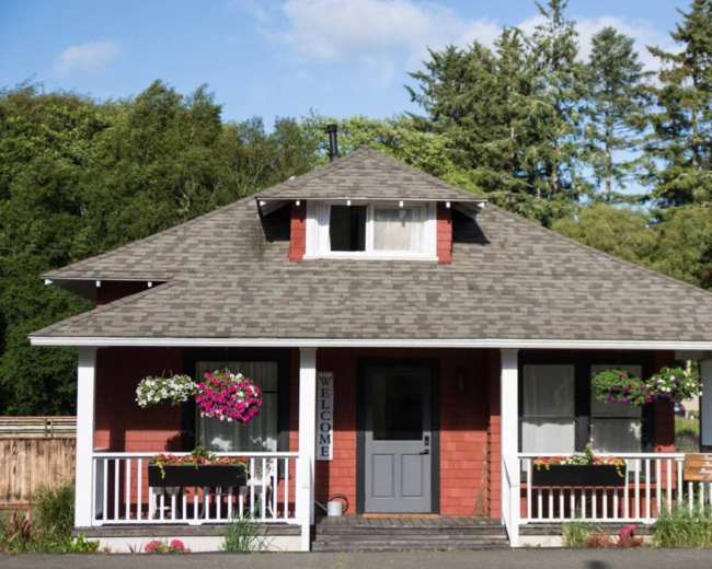 A red and white house with a gabled roof and a welcoming front porch is surrounded by greenery.